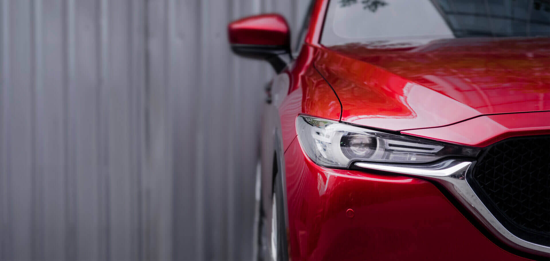 Close Up Headlight Of Red Car Against Gray Blurred Background.